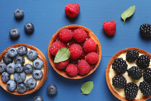 istock Tartlets with different fresh berries on blue wooden table, flat lay. Delicious dessert 1900997619