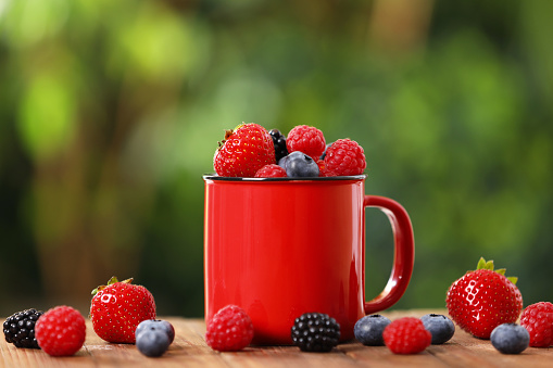 Mug with different fresh ripe berries on wooden table outdoors