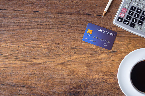 Top view of a blue credit card, pencil, calculator, coffee cup on wooden table in office. Space for text. Wood texture background. Business and finance concept