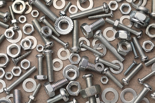 Different metal bolts and nuts on beige textured table, flat lay