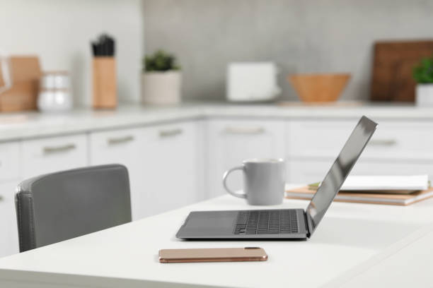 istock Home office. Laptop, smartphone, cup and stationery on white desk in kitchen, space for text 1901122047