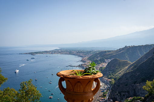 Decorative clay Amphora pot with succulent plants with Taormina aerial view in the background