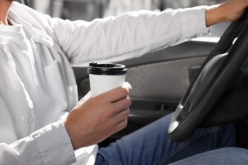 Coffee to go. Man with paper cup of drink driving his car, closeup