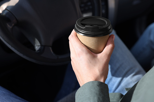 Coffee to go. Man with paper cup of drink in car, closeup