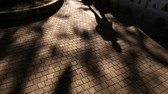 Monochromatic, silhouette legs and long shadows across an ancient cobbled street in early evening setting sunlight