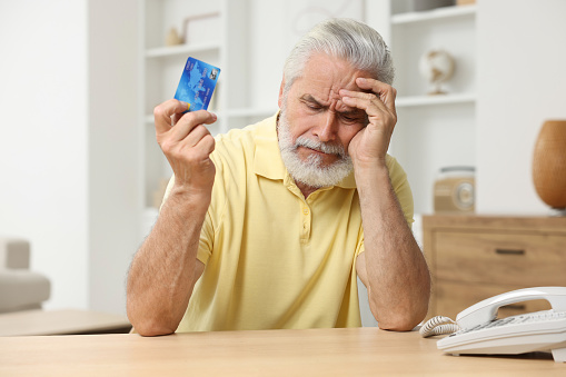 Unhappy senior man with credit card at home. Be careful - fraud