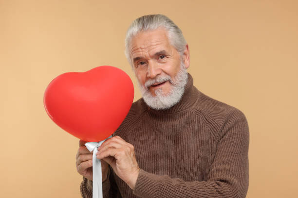 istock Senior man with red heart shaped balloon on beige background 1901198687