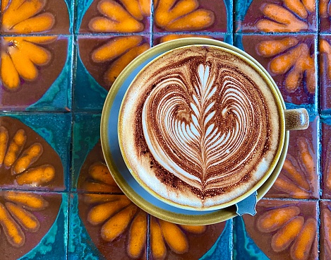 Horizontal flat lay of cafe culture coffee cup art with saucer and teaspoon on ceramic glazed tiles in vintage orange brown and blue flower pattern at cafe in country Australia