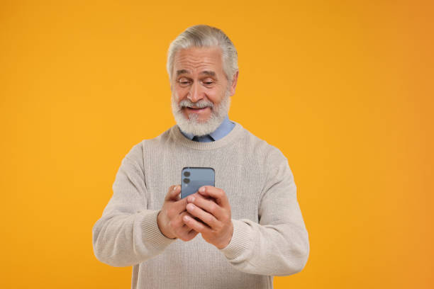 istock Happy senior man using smartphone on yellow background 1901200228