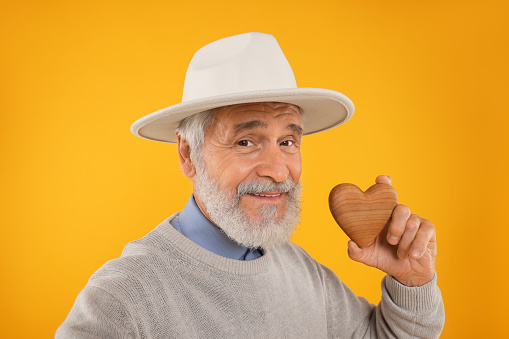 Senior man with wooden heart on yellow background