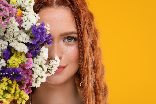 Beautiful young hippie woman and bouquet of colorful flowers on orange background, closeup. Space for text