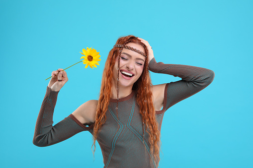 Beautiful young hippie woman with sunflower on light blue background