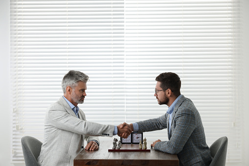 Men shaking their hands during chess tournament at table indoors