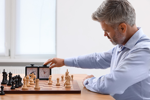 Man turning on chess clock during tournament at table indoors