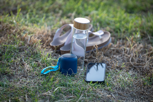 essentials for summer holidays sandals, water , wireless speaker and a mobile