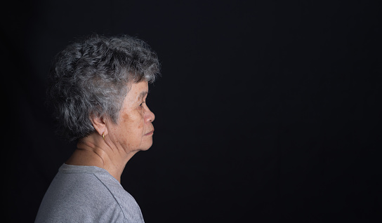 Side view of a senior woman with short white hair looking away with a smile while standing on a black background in the studio. Space for text. Aged people and relaxation concept