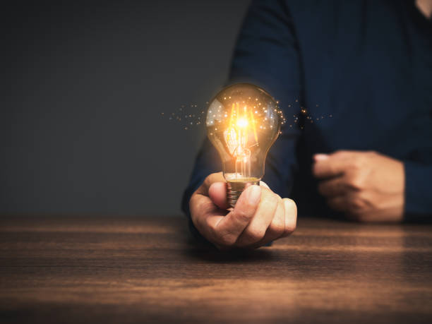 istock Innovative business ideas. Hand of a man holding a lighting bulb with lighting while sitting at the table. 1901397804