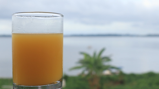 Glass of orange juice on table next to the beach.