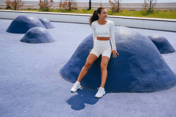 istock Active woman in a white outfit taking a break and leaning on a blue exercise mound at an outdoor fitness park 1901495077
