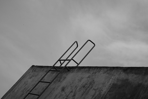 Monochrome Photography. Black and white photo of a house roof wall with an iron ladder. An iron ladder is installed on the wall for access to the rooftop. Bandung, Indonesia