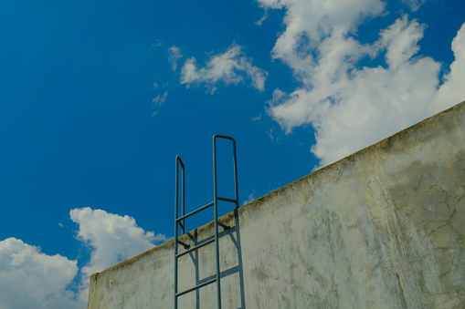 Background Photography. A roof wall of a house with an iron ladder. Iron ladder against brick wall leading to blue cloudy skies. Bandung, Indonesia