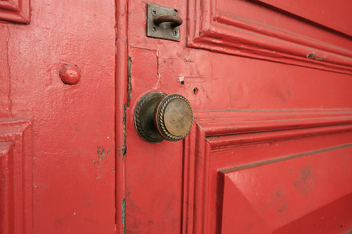 Close-up on part of an old dirty wooden red door with a brass knob.