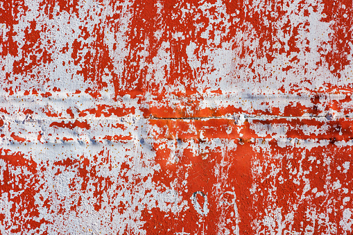 red welded steel sheet wall with peeled off white paint under direct sunlight, full-frame background and texture.