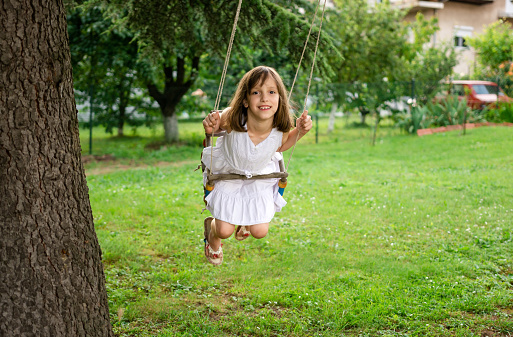 Happy little girl is swinging on a swing in the yard during a summer day.