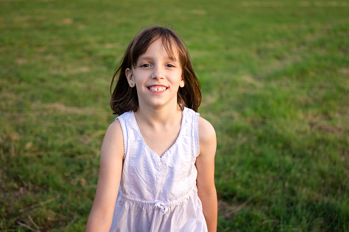 A happy girl is walking in a meadow during a summer day and looking at camera.