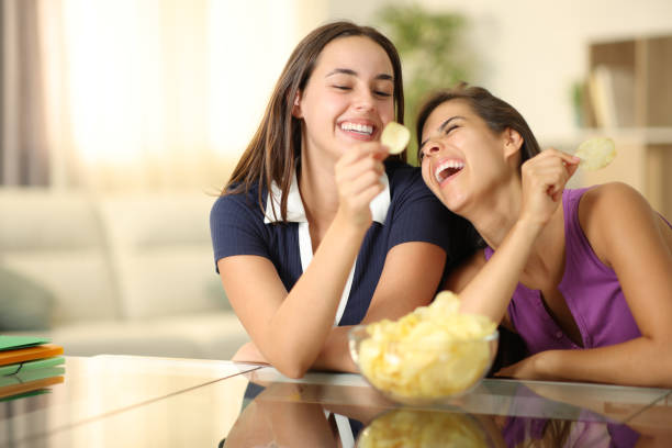 Two funny roommates laughing and eating potato chips