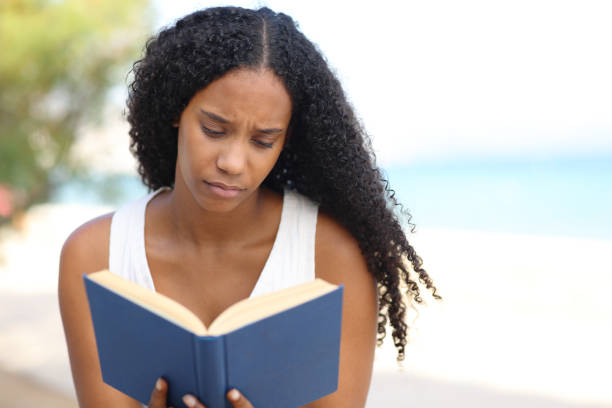 Serious black woman reading a paper book on th beach