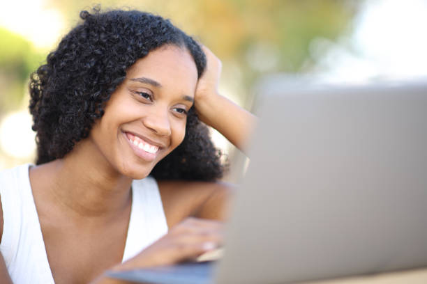 Happy black woman using laptop outside