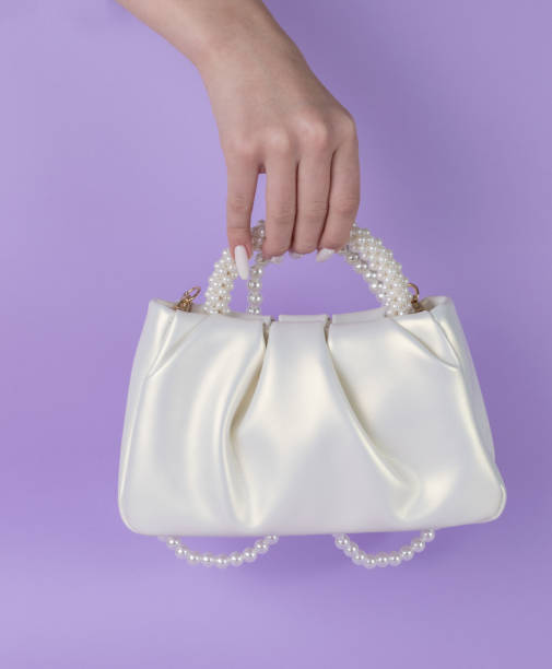istock A woman's hand with a white handbag on a purple background. 1901708420