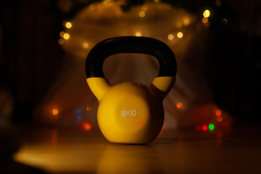 Yellow kettlebell in front of Christmas lights on living room floor, dark and moody, new year resolution concept