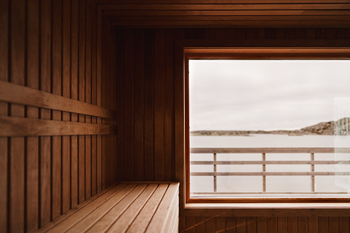 Photograph of the inside of an empty dry sauna with large windows. Walls and benches made of wood and a tile floor.