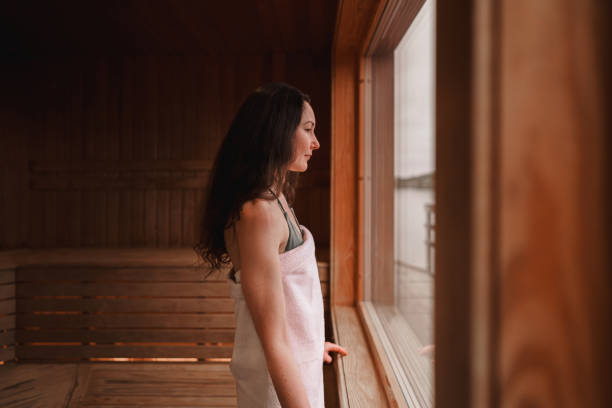 Woman enjoying the view from a dry sauna Photograph of the inside of an empty dry sauna with large windows. Walls and benches made of wood and a tile floor. A woman is standing by the large window, looking out at the view of the Swedish west coast. swedish sauna stock pictures, royalty-free photos & images