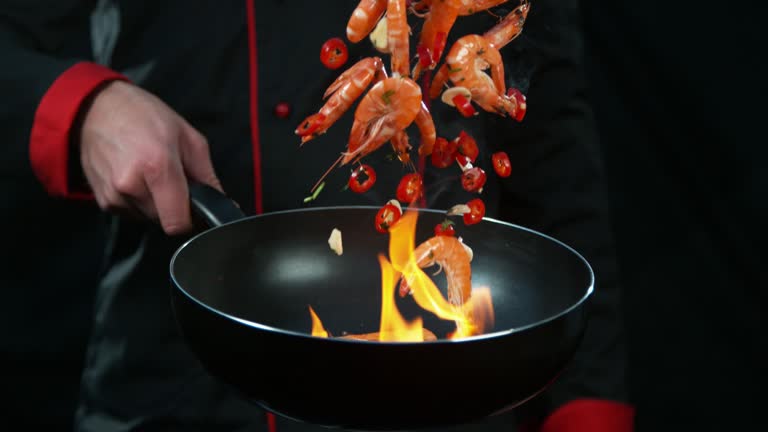 Super slow motion of chef holding frying with flying prawns.