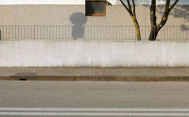istock Fence made of white plaster wall with railing on top. House wall on behind. Cement tiled sidewalk and street in front. 1901764867