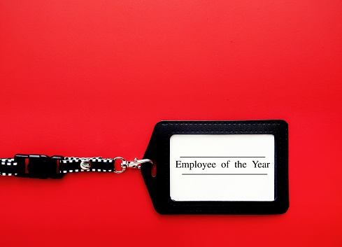 Employee staff ID card  with text written EMPLOYEE OF THE YEAR on red background, refers to excellent outstanding talented employee, badge of honor give employees to recognize efforts and contribution