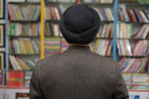 Portrait of smiling sardar sikh male college student standing in a library. Front and back portrait of a man in library.