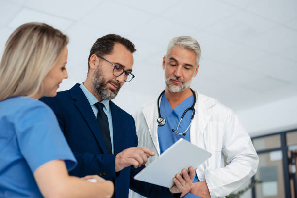 istock Pharmaceutical sales representative talking with doctors in medical building, presenting them new product on tablet, business talk. Hospital director consulting with healthcare staff. 1901785628