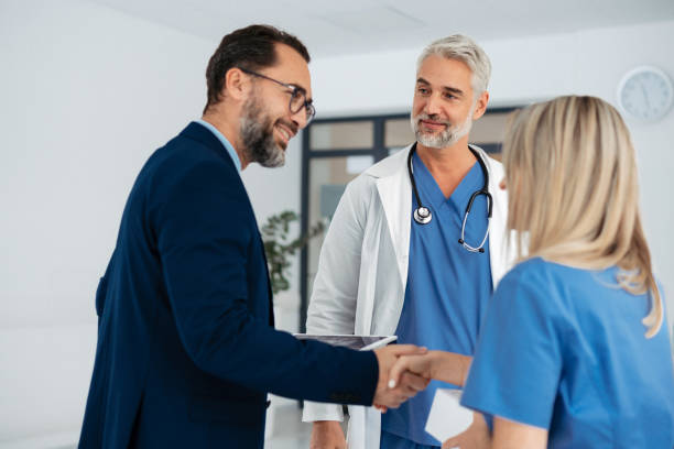 istock Pharmaceutical sales representative talking with doctors in medical building, convicing her to try new pharmaceutical product, shaking hands. Doctor holding box with drug samples. 1901788222