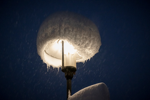 Street lamp with bonnet made of fresh snow during heavy snowfall at night, Bavaria, Germany