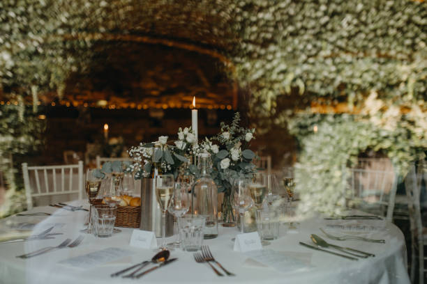 istock Elegant, romantic table setting for indoor wedding reception with fairy lights on wall behind. Luxury wedding table decoration, special event table set up with fresh flowers arragements. 1901808835