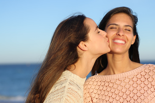 Happy woman kissing a friend on cheek on the beach