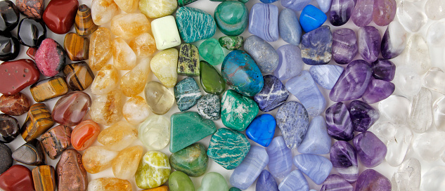 Rows of tumbled polished healing crystal laid out in chakra colours white, purple, blue, turquoise blue, green, yellow, orange, red ideal for crystal healing theme