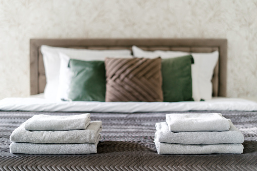 Selective focus on clean bath towels neatly folded on comfort double bed with pillows and blanket in cozy hotel room. Detail in interior. Rest and relax concept. Contemporary bedroom