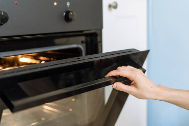 mão da mulher porta aberta do forno elétrico para preparar o jantar na cozinha - home interior women domestic kitchen cabinet - fotografias e filmes do acervo