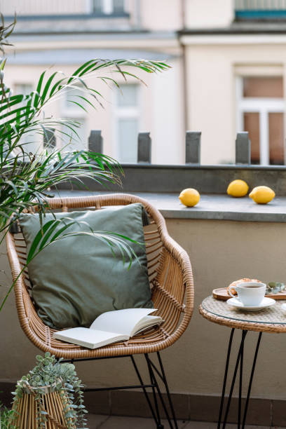 Vertical shot of rattan armchair next to coffee table on terrace of cafe Vertical shot of rattan armchair with green cushion and diary journal or paper book for reading next to coffee table with cup on terrace of cafe in city center. Place for relax and having breakfast apartment balcony garden stock pictures, royalty-free photos & images