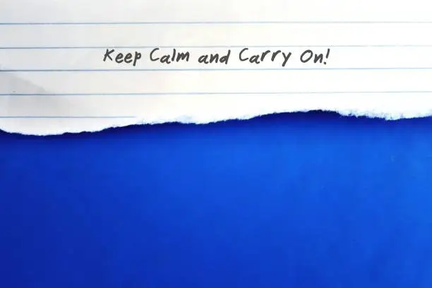 Photo of Torn note on copy space blue background with text KEEP CALM AND CARRY ON,  self reminder to set peace of mind, let go all stress and anxiety , aiming to goal with inner strength and self confidence